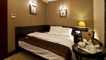 A hotel room with a large bed, a bedside table with a lamp, and a small table with a tea set.