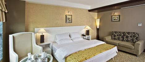 A hotel room with a bed, a sofa, a small table with a tray of breakfast items, and two wall-mounted lamps.