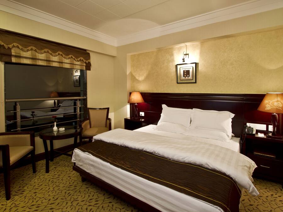 Una habitación de hotel con una cama grande, dos mesitas de noche con lámparas, un escritorio con silla y un minibar.
