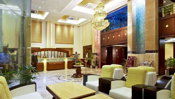A hotel lobby with a reception desk, seating area, and a chandelier. - Gargee Grand Patna (Patna)