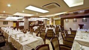 A spacious dining area with multiple tables set for guests, featuring a modern chandelier and a large pillar. - Gargee Grand Patna (Patna)