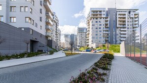 A modern urban street with multi-story residential buildings, a paved road, and a landscaped area with flowers. - Rent a Flat Apartments - Jana Pawla II (Gdansk)