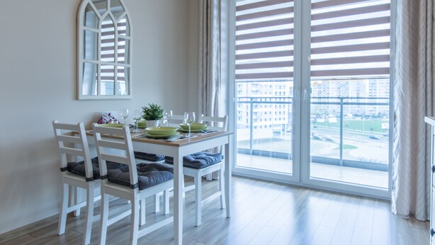 A dining area with a table set for four, a large window with blinds, and a view of a cityscape. - Rent a Flat Apartments - Jana Pawla II (Gdansk)