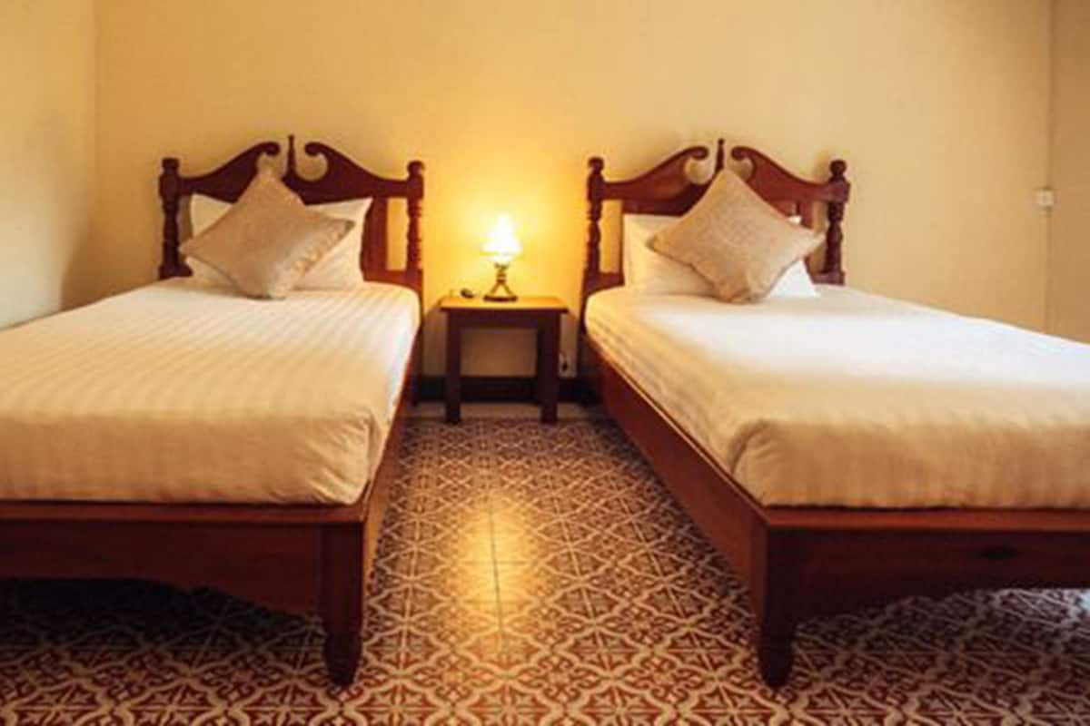 Une chambre avec deux lits simples, une petite table de chevet avec une lampe et des carreaux de sol à motifs.