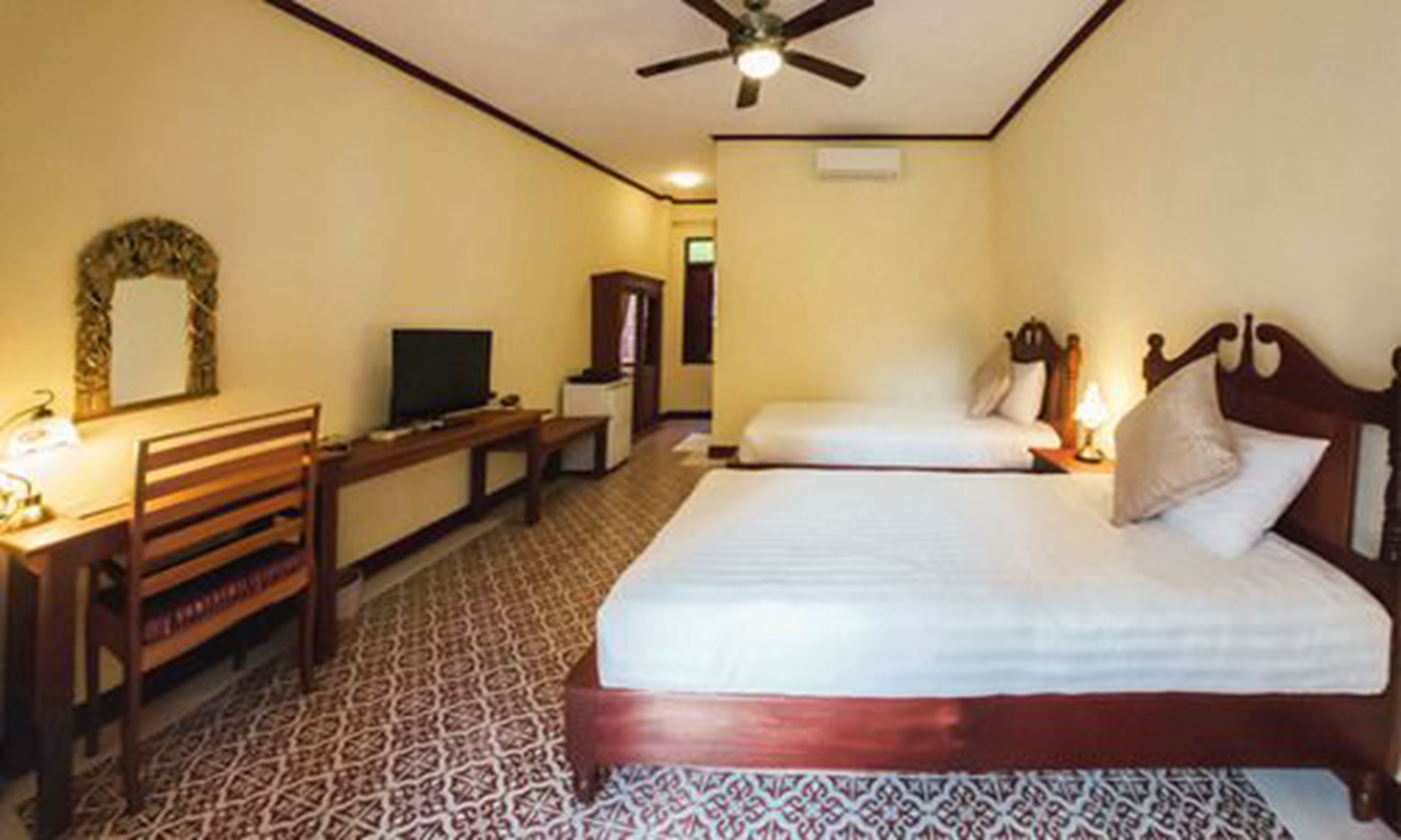 Une chambre d’hôtel avec un lit, un bureau avec une télévision, une chaise et un tapis à motifs.