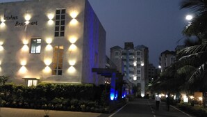 A building with the name 'Krishna Restaurant' illuminated at night, surrounded by other buildings and a pathway. - Om Leisure Resort Puri (Brahmagiri)
