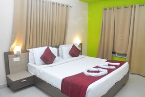 Habitación de hotel con cama, cortinas, mesita de noche y una lámpara de pared.