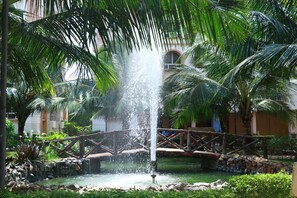 Una fuente con chorros de agua, rodeada de palmeras y un puente de piedra.