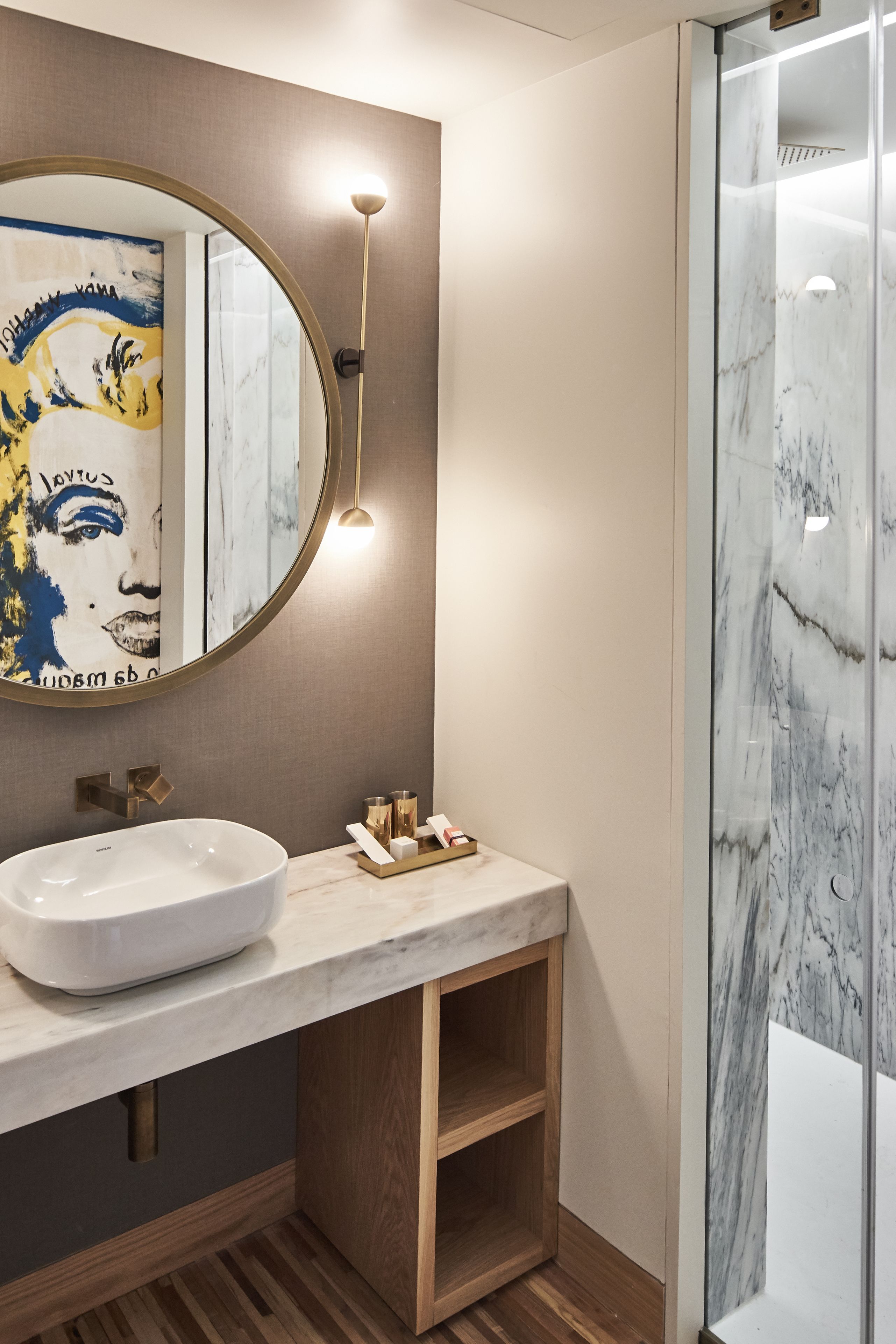 Une salle de bain moderne avec un grand miroir rond, un lavabo blanc et une douche à l’italienne en marbre.