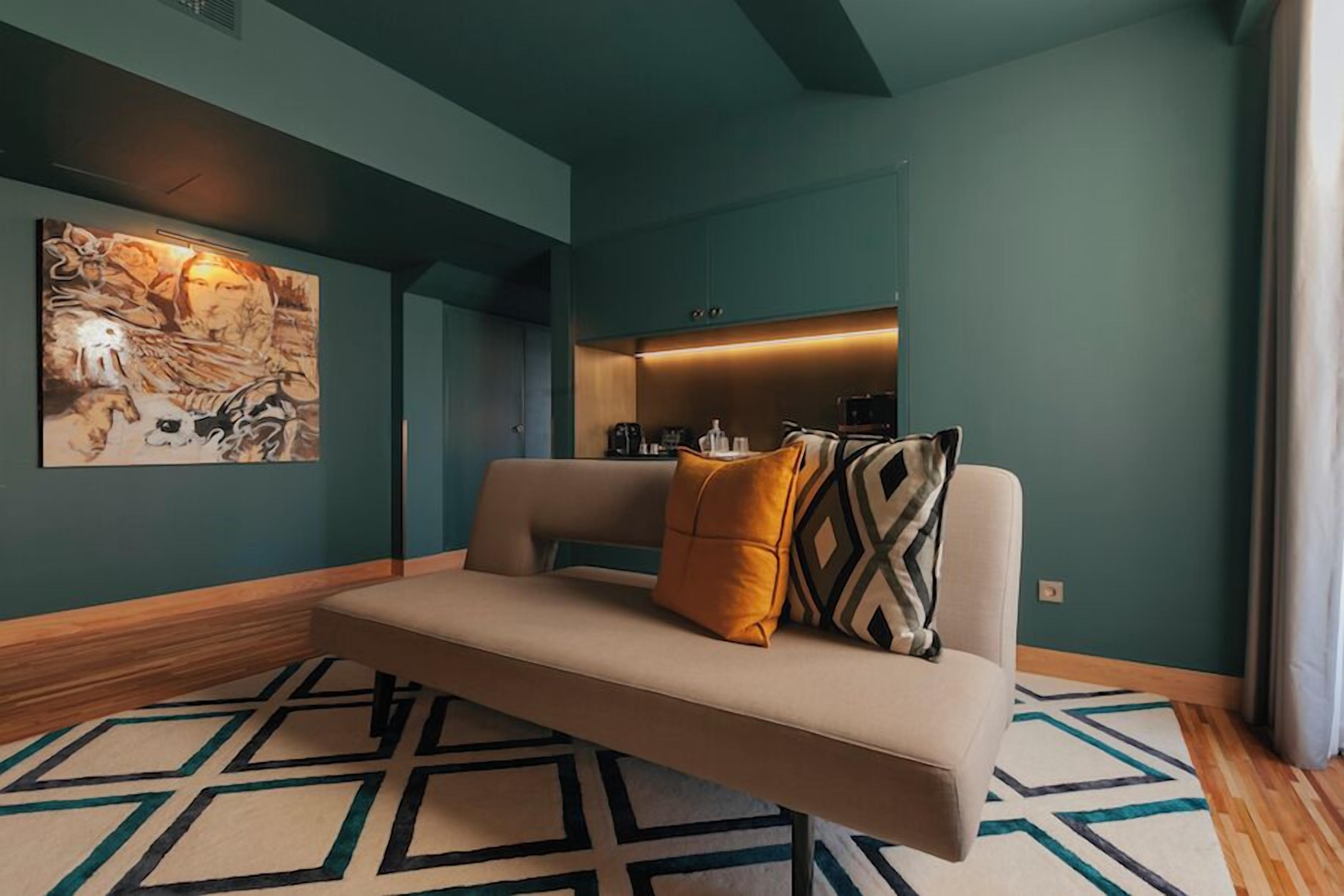 A modern living room with a sofa, a geometric patterned rug, a wall-mounted artwork, and a built-in kitchen area.