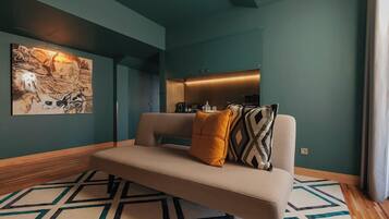 A modern living room with a sofa, a geometric patterned rug, a wall-mounted artwork, and a built-in kitchen area.