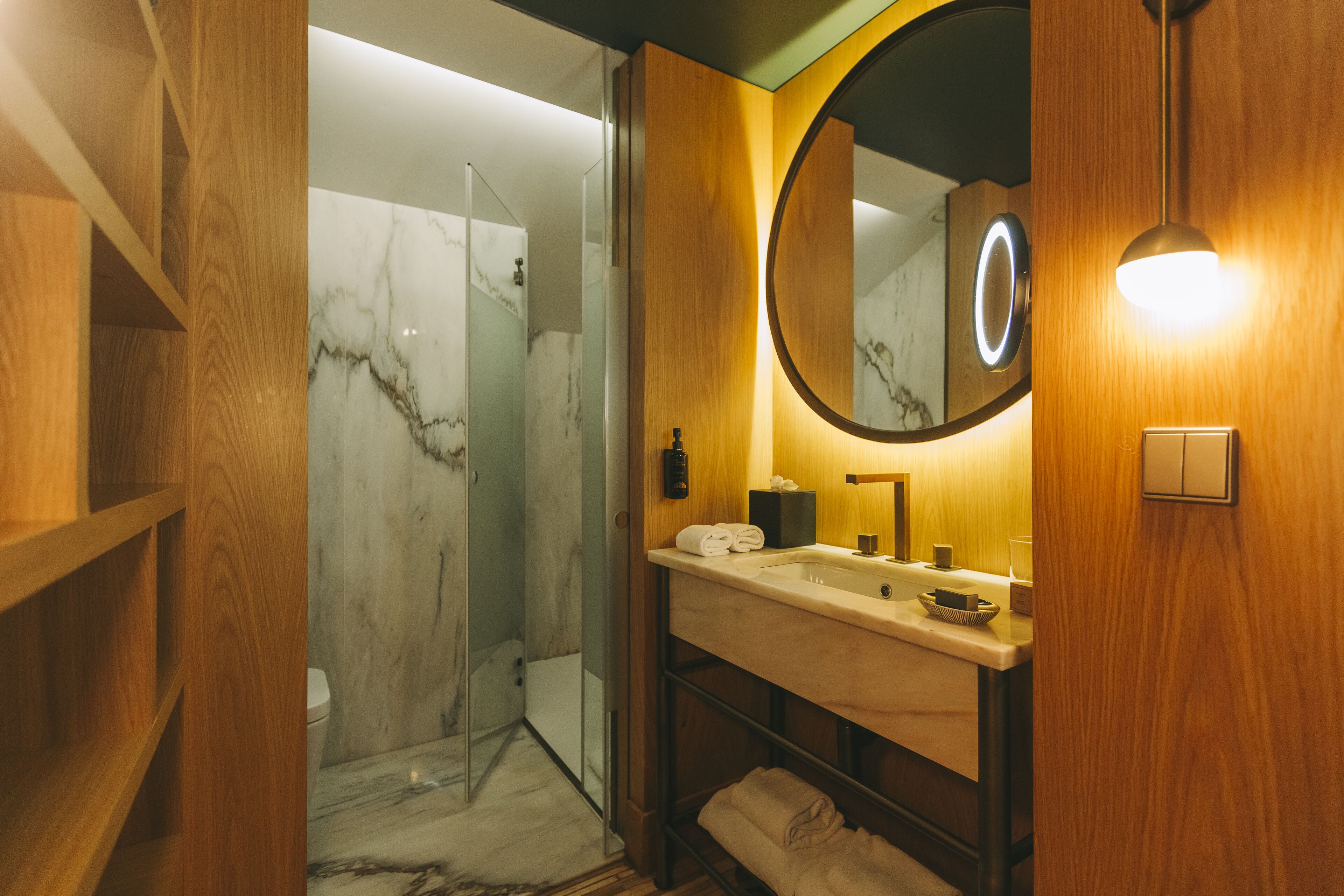 A modern bathroom with a wooden vanity, a glass shower enclosure, and a marble-tiled floor.