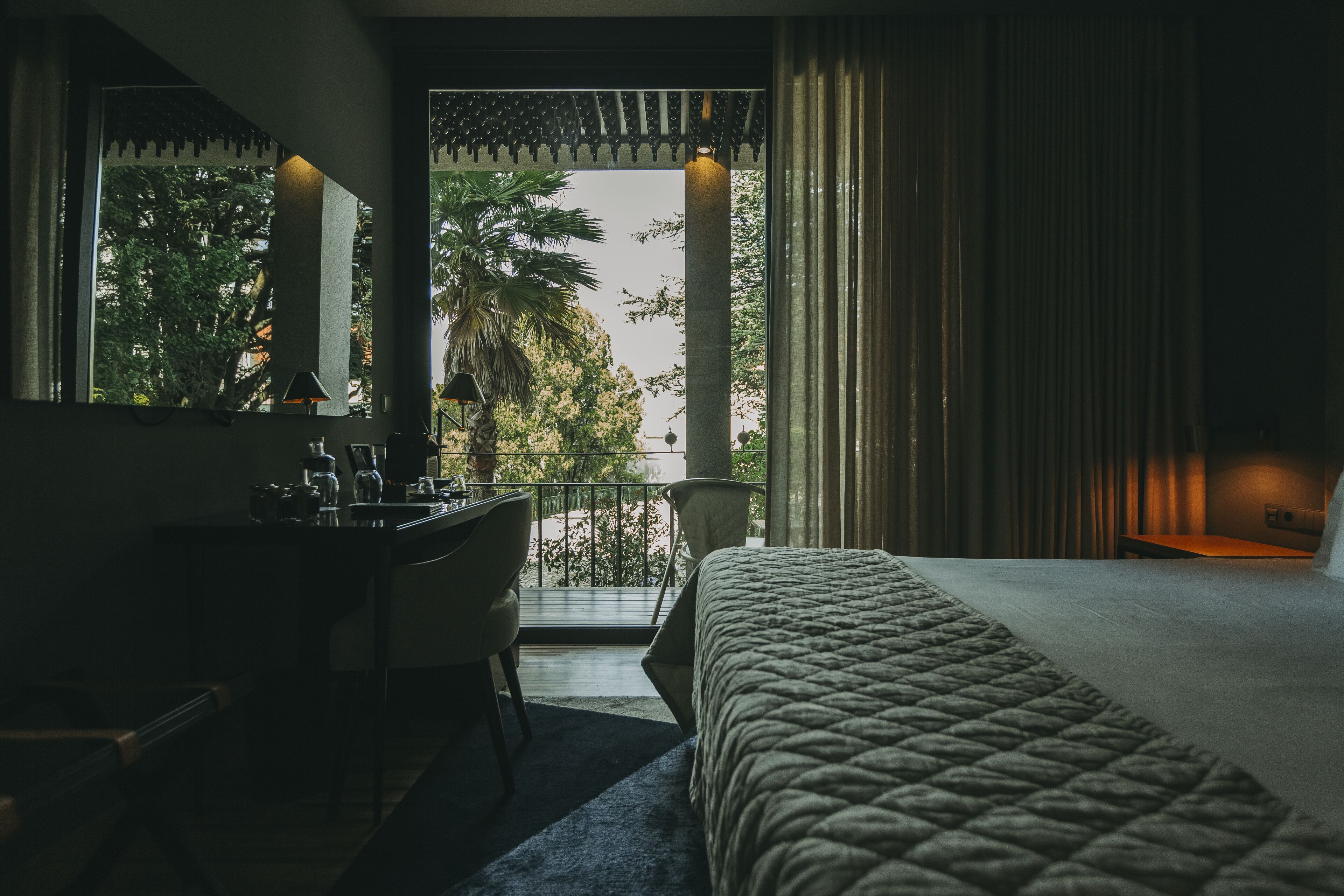 Habitación de hotel con cama, escritorio y balcón con vista a palmeras.