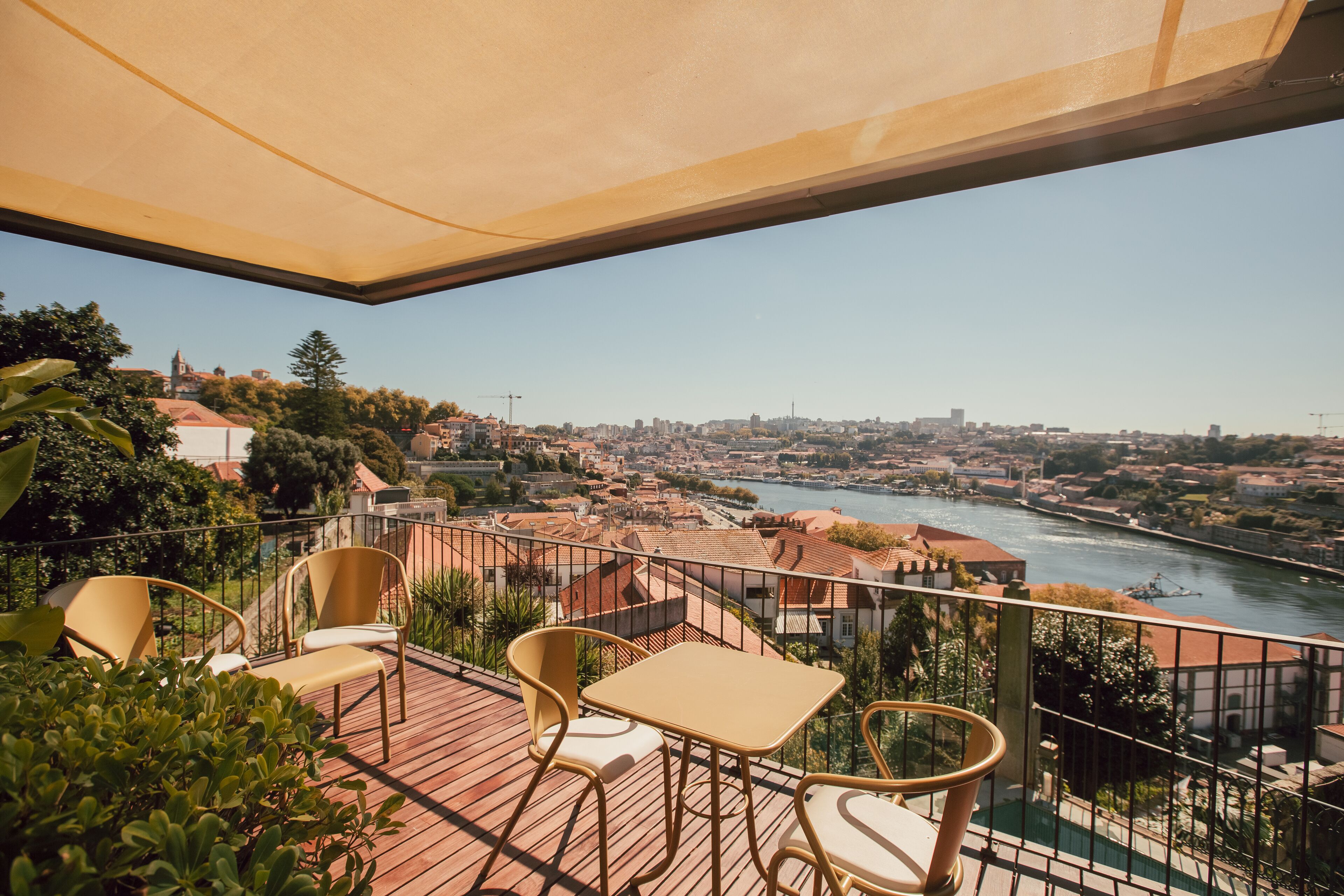 Une terrasse avec une table et des chaises, d’où l’on a vue sur une rivière et sur le paysage urbain.