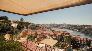Une terrasse avec une table et des chaises, d’où l’on a vue sur une rivière et sur le paysage urbain.