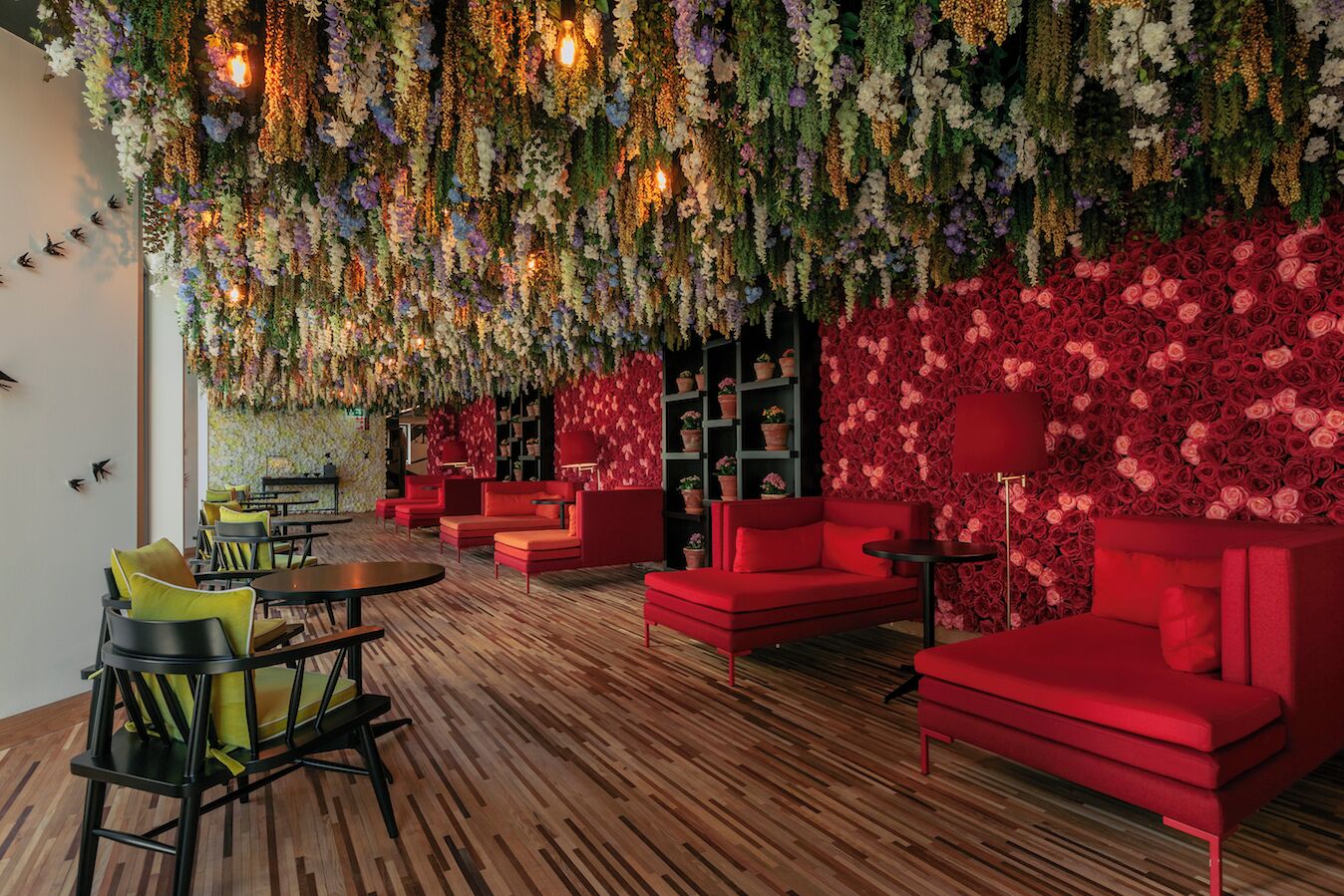 A modern lounge area with red sofas, wooden flooring, and a floral wall.