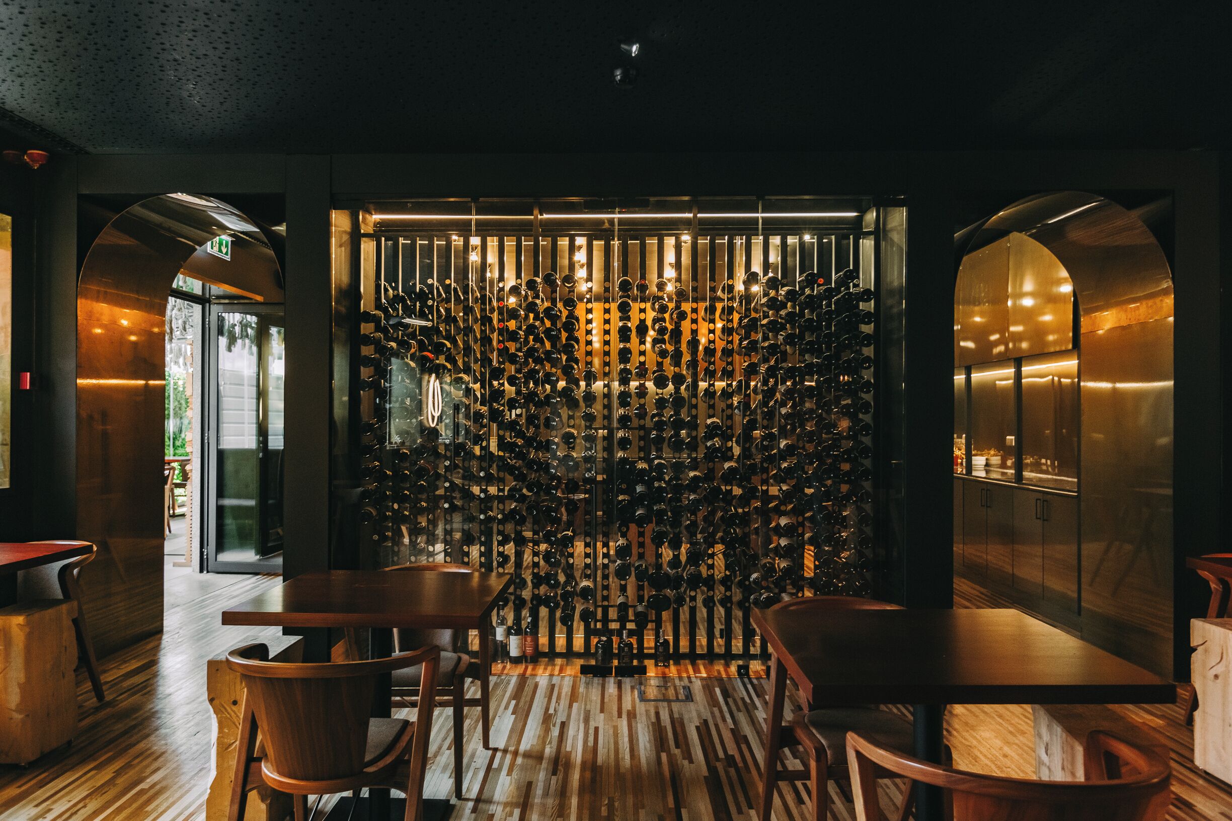A restaurant interior with wooden flooring, a wall of hanging wine bottles, and a glass partition.