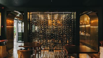 Un interior de restaurante con suelo de madera, una pared decorada con botellas de vino colgantes y un separador de vidrio.