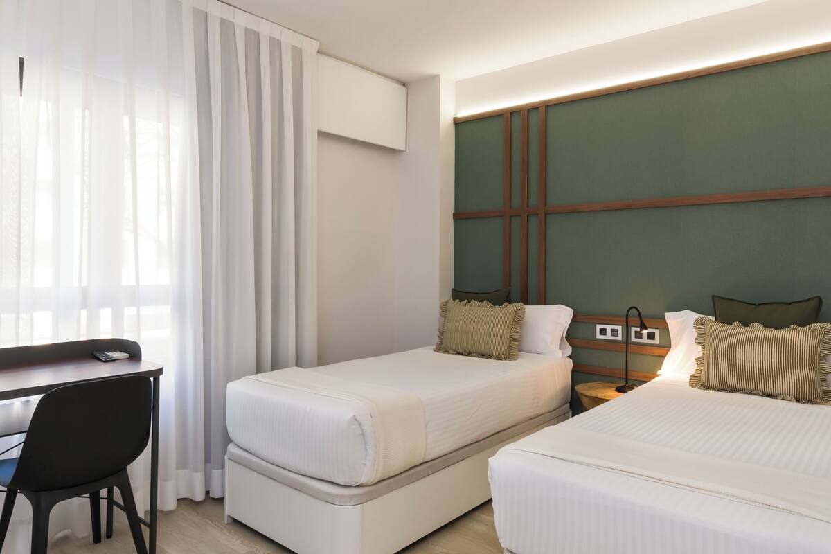Ein Hotelzimmer mit zwei Einzelbetten, einem Schreibtisch und einem Stuhl.