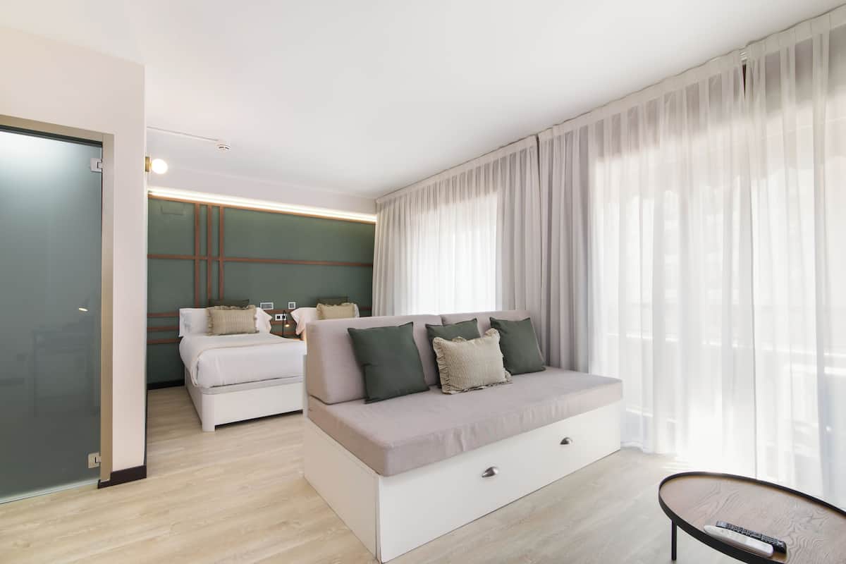 Ein modernes Schlafzimmer mit Schlafsofa, einem separaten Bett und einer Glastrennwand.