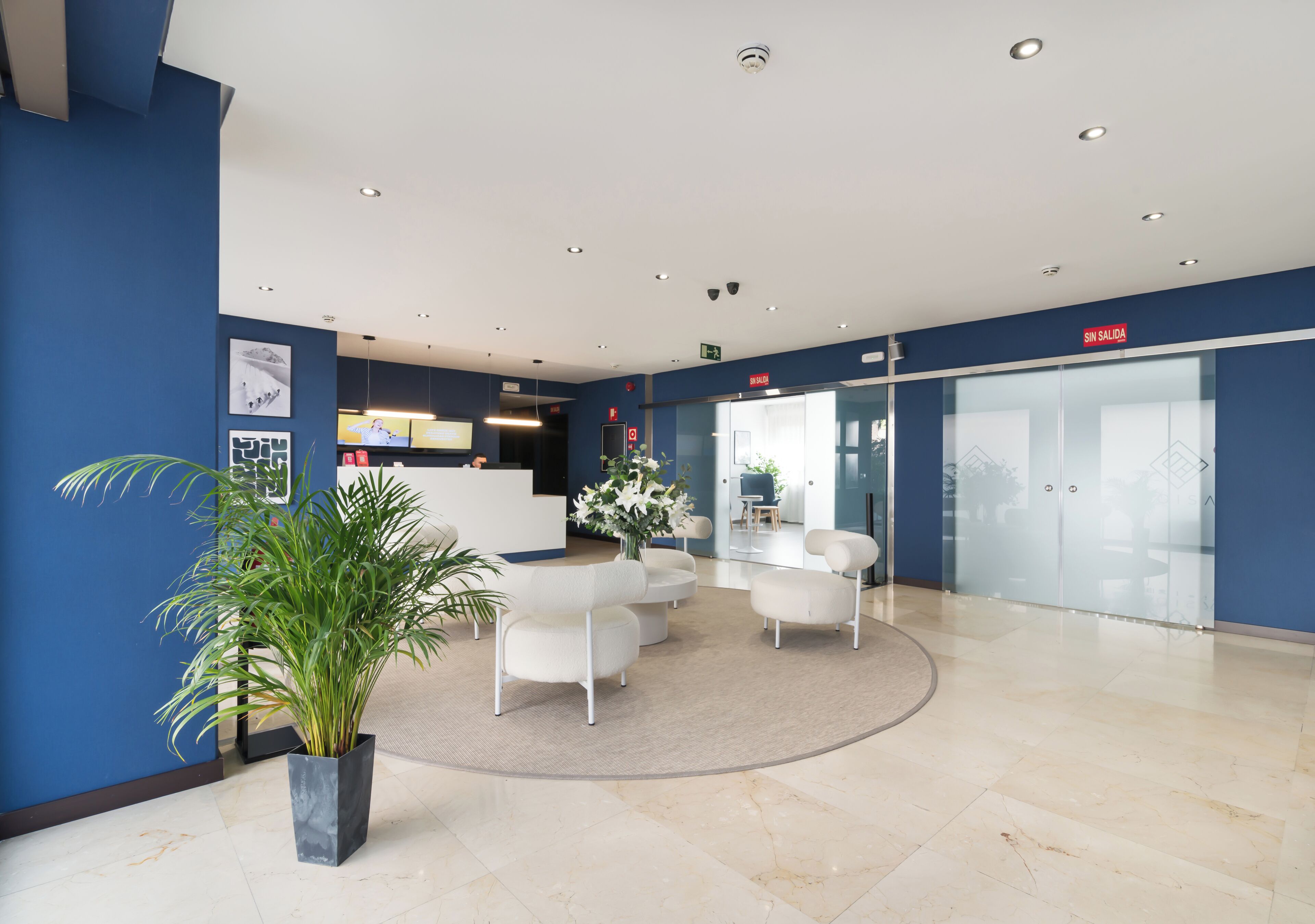A modern lobby with a reception desk, seating area, and a glass wall with a sign.