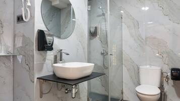 Un baño moderno con pared de mármol, ducha con cerramiento de vidrio, lavabo blanco y retrete.