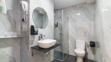 Un baño moderno con pared de mármol, lavamanos blanco, cabina de ducha de vidrio y un inodoro.