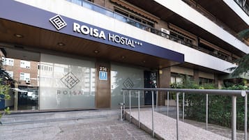 Exterior de un hotel de diseño moderno llamado ROISA HOSTAL, con un logotipo destacado y señal de accesibilidad para sillas de ruedas.