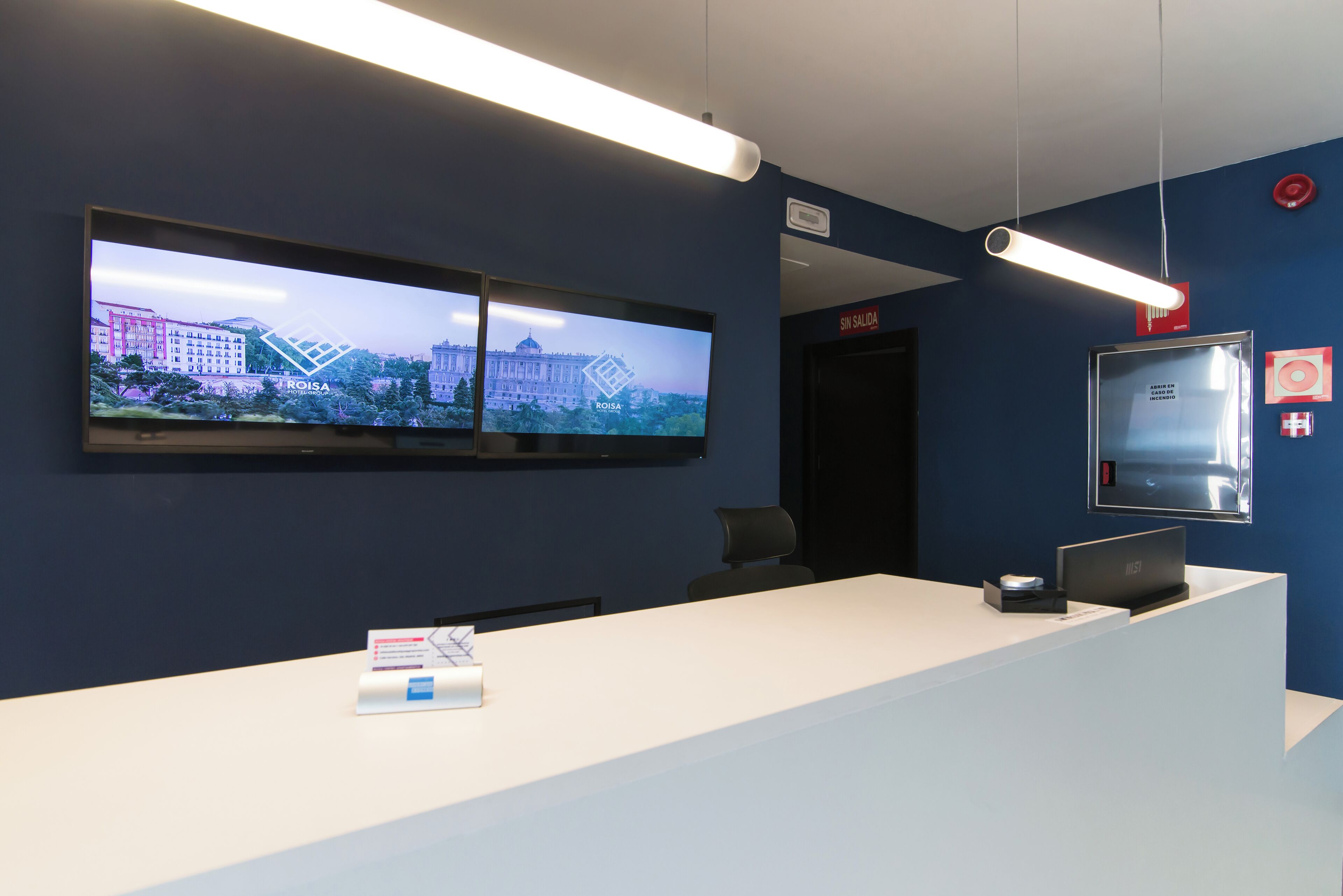 A reception area with a flat-screen TV displaying a cityscape, a reception desk, and a sign indicating the exit.
