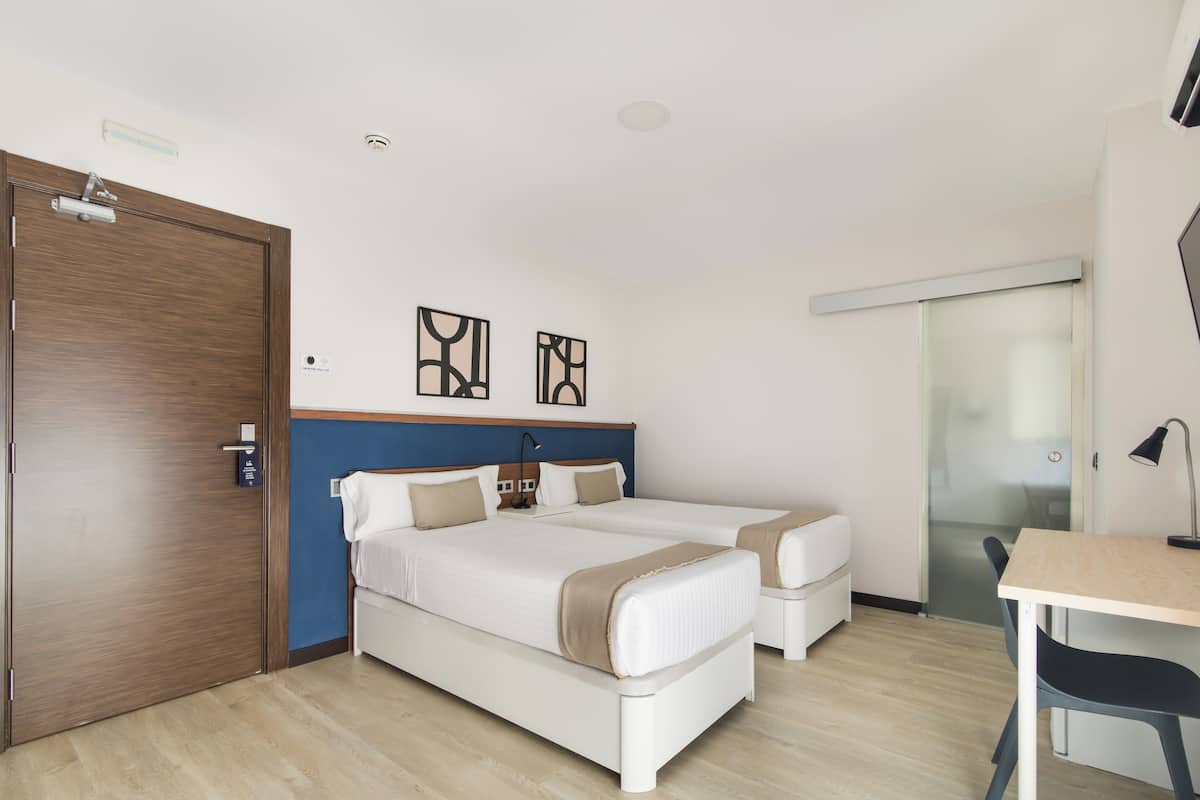Ein Hotelzimmer mit zwei Betten, einem Schreibtisch und einer Schiebetür.