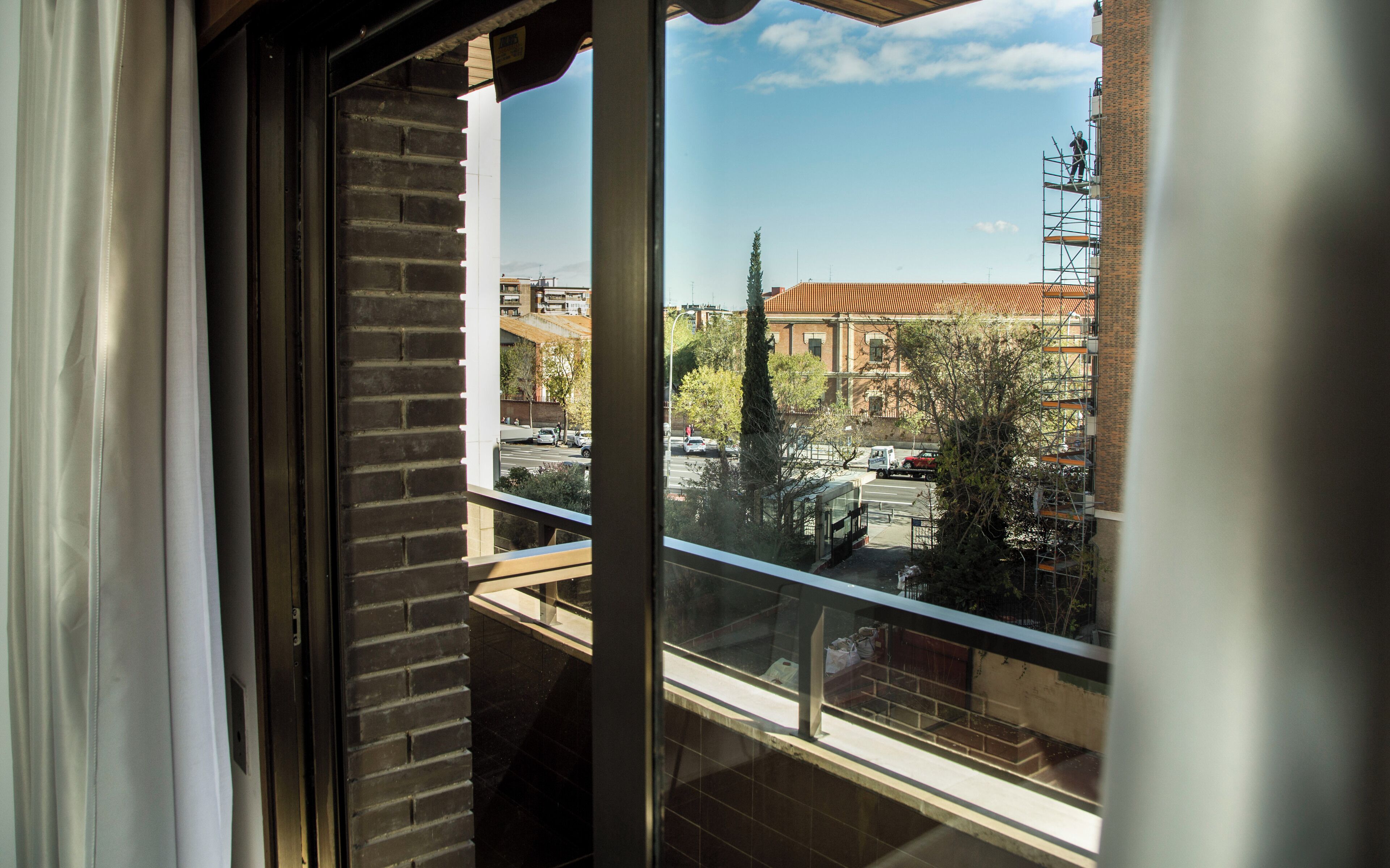 Vista desde una ventana con baranda de metal, que da a una calle con edificios y árboles.