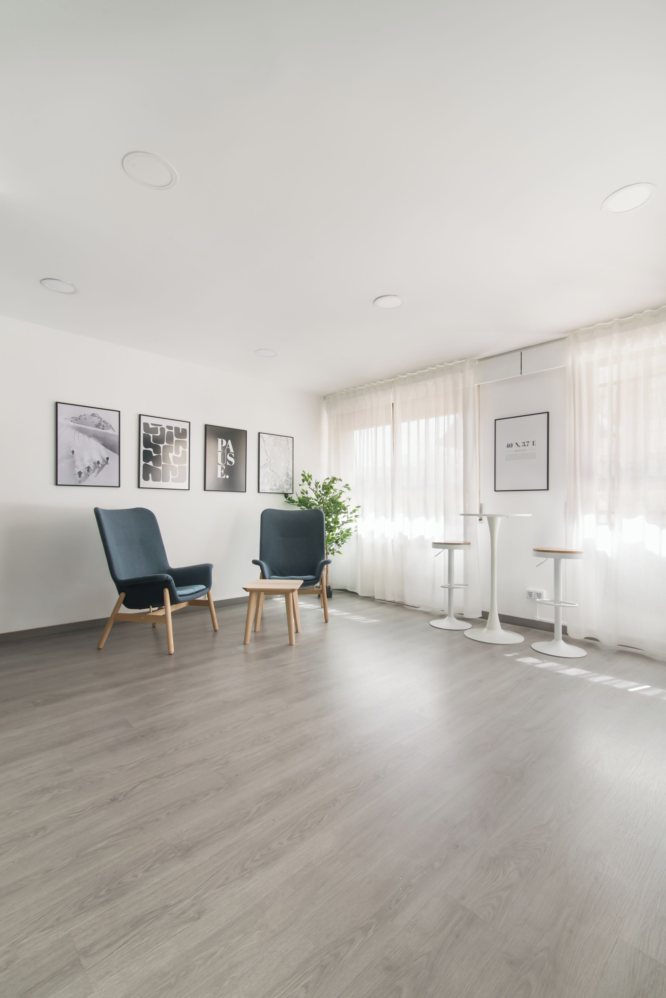 Una habitación amplia con dos sillas azul oscuro, una planta en maceta y tres mesitas auxiliares blancas.