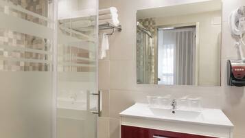 A modern bathroom with a glass shower enclosure, a white sink with a red cabinet, and a hairdryer mounted on the wall.