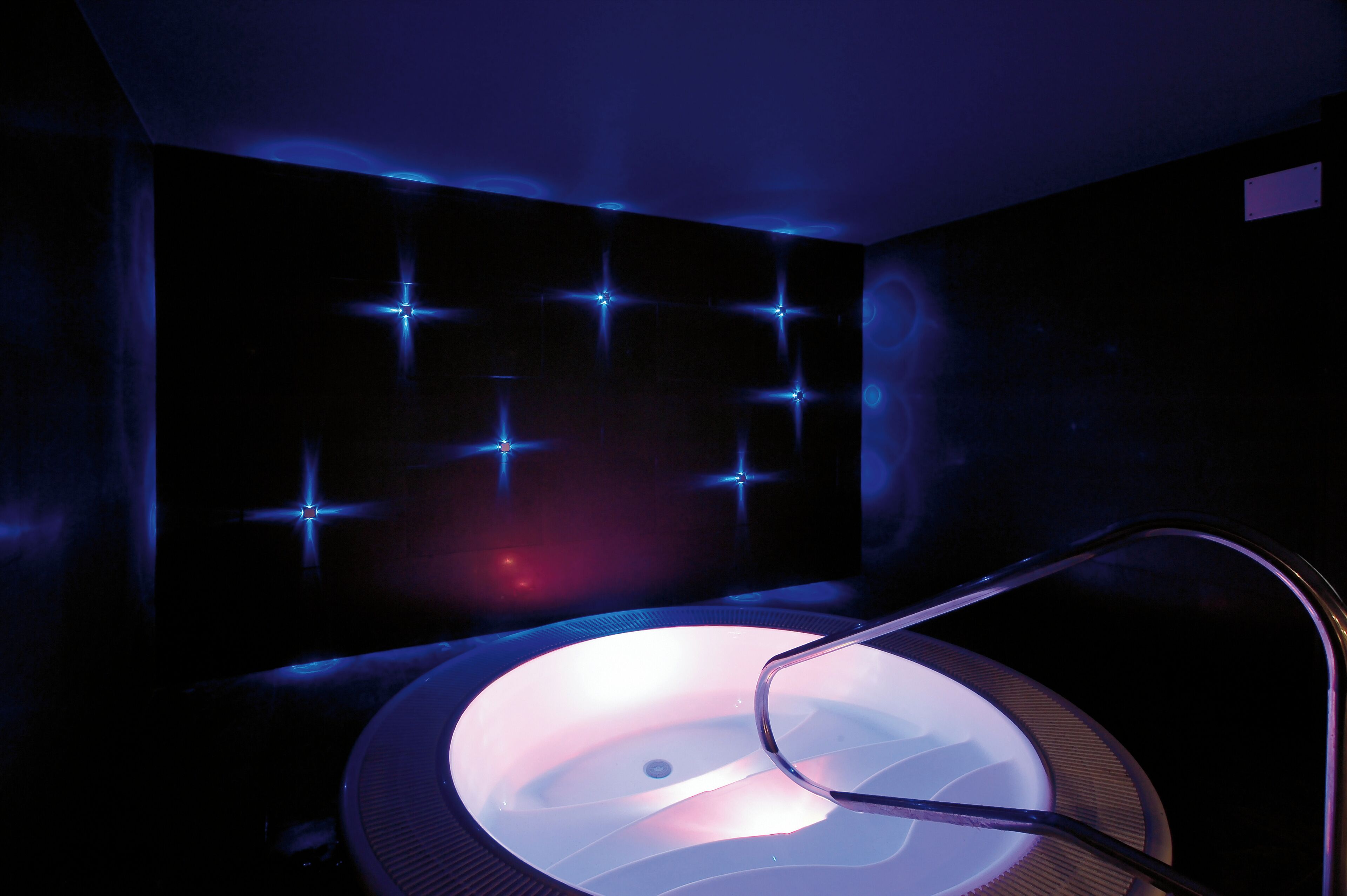 A dimly lit room with a circular hot tub and a metal chair.