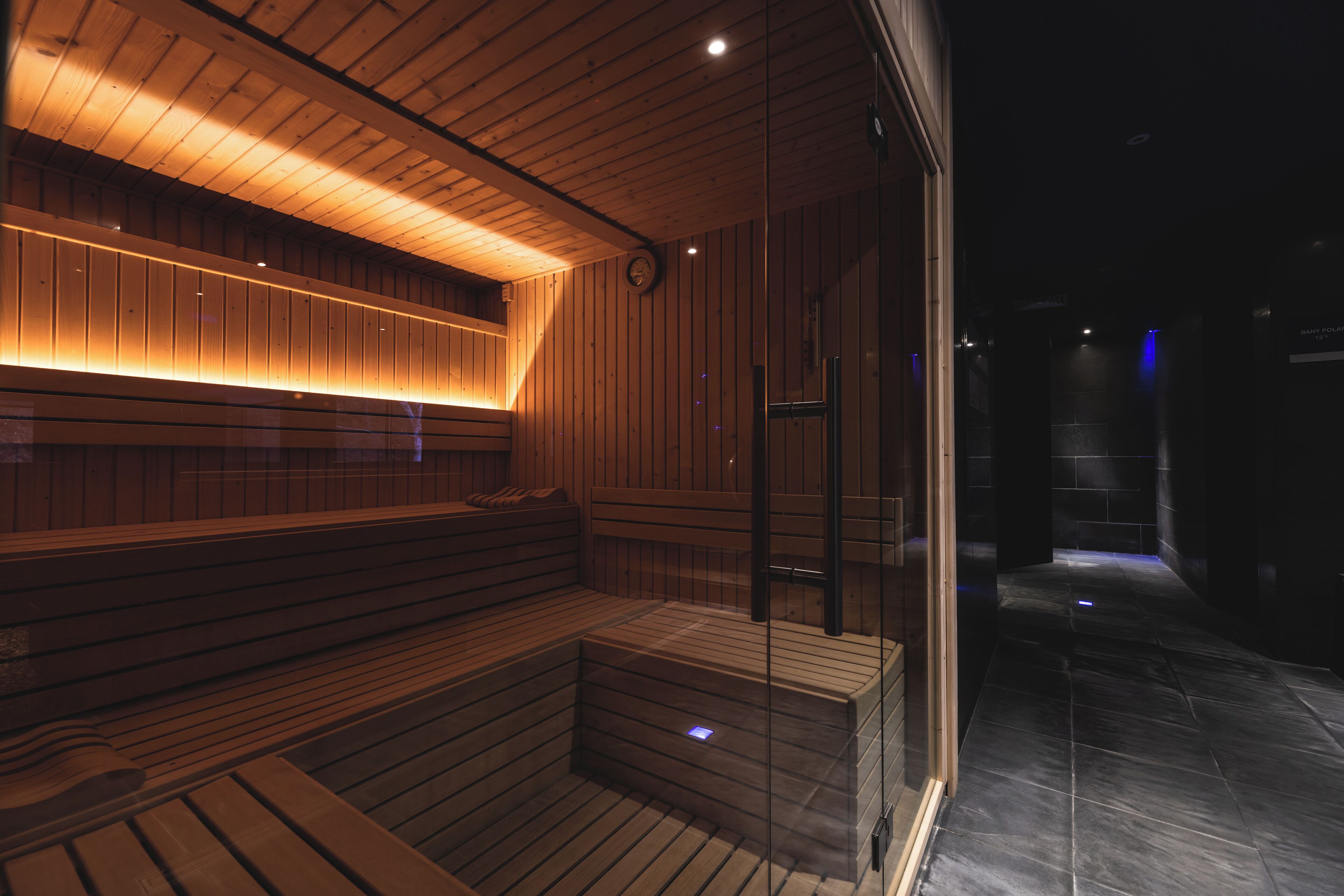 Una sauna de madera con bancos y puerta de vidrio, con techo de madera y suelo de baldosas.
