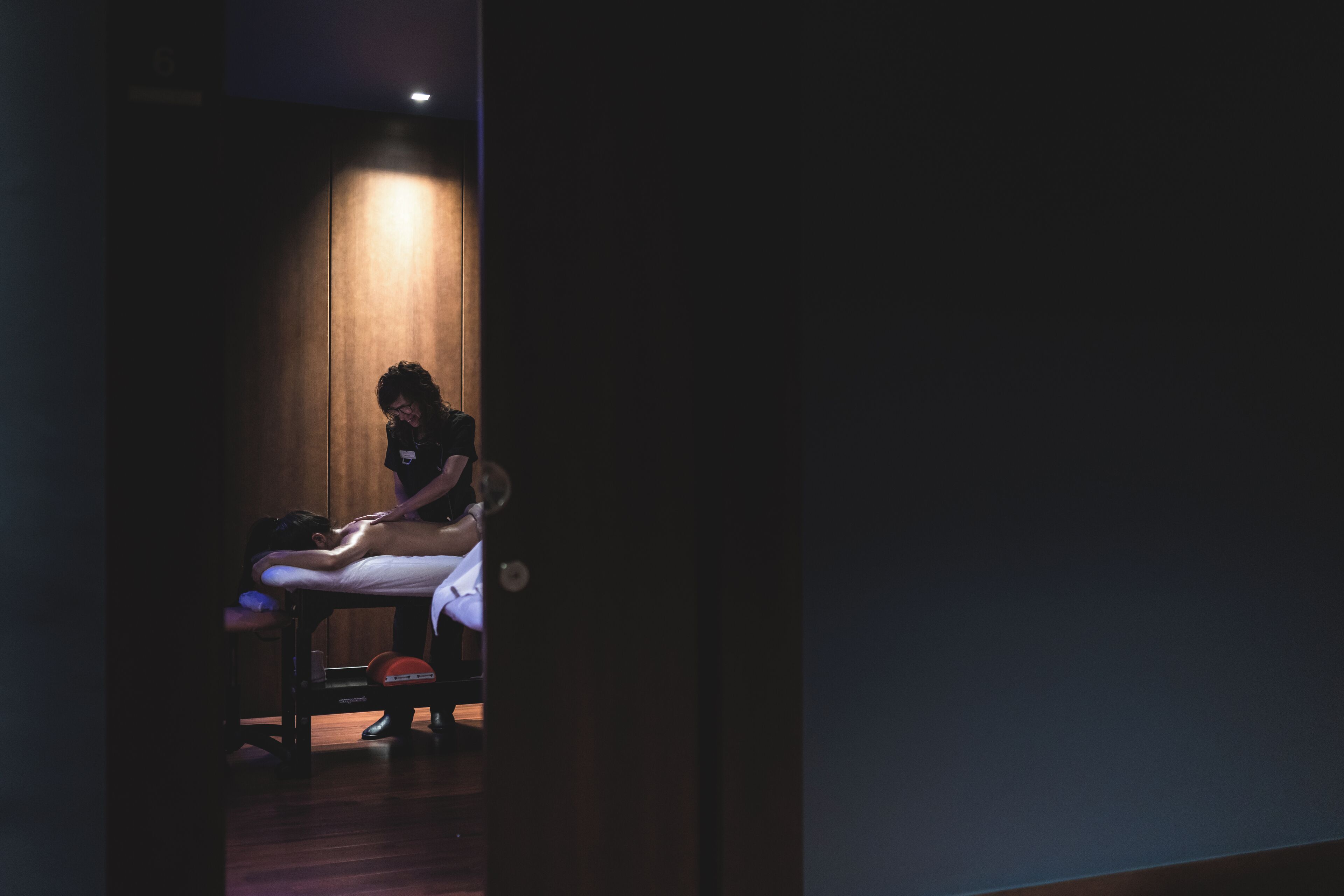 A massage therapy room with a wooden floor, a massage table, and a single massage therapist.