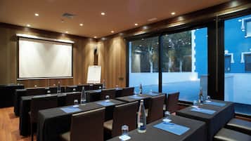 A conference room with tables, chairs, a projector screen, and a large window with a view of the outside.