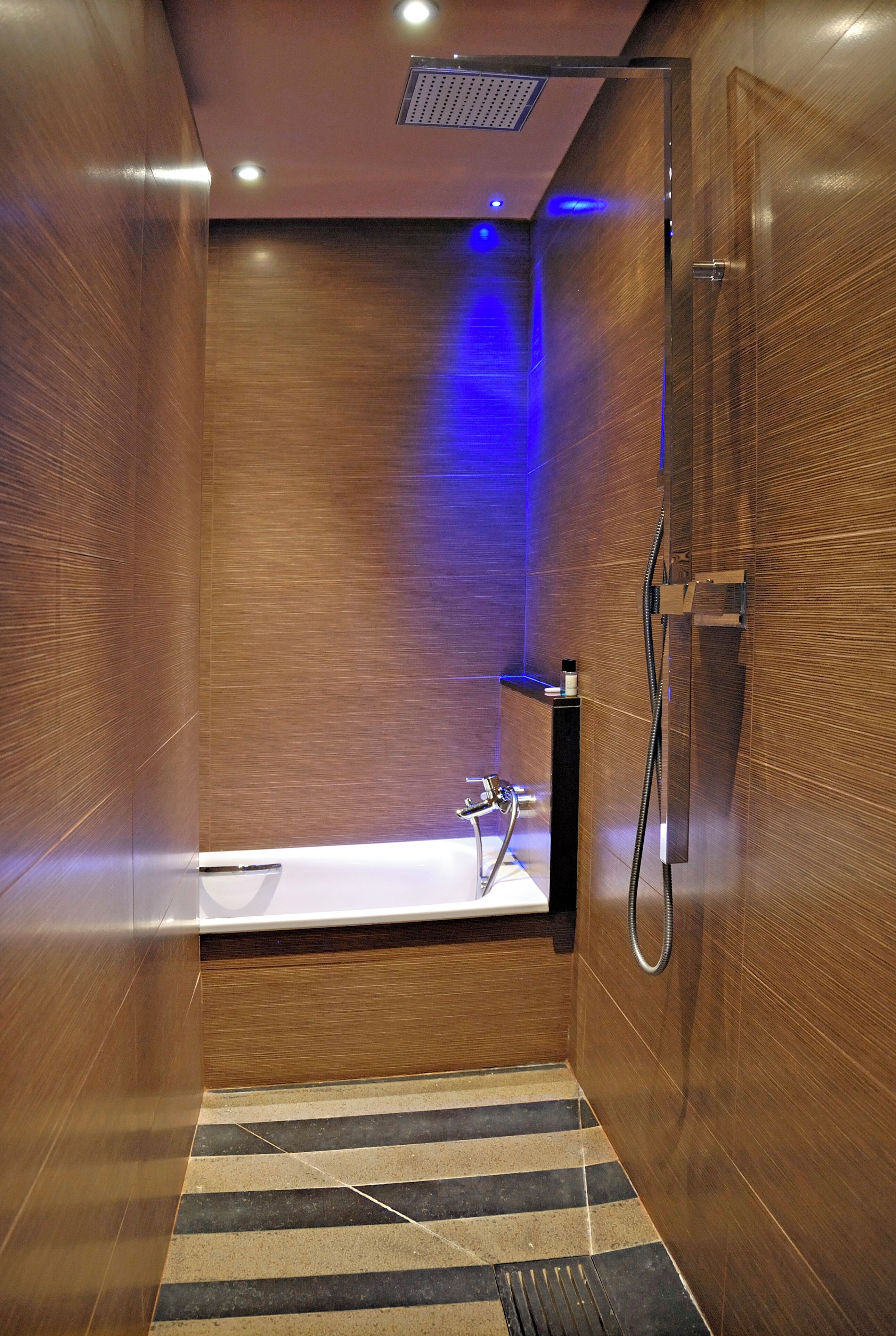 Un baño moderno con detalles de madera, una bañera, una ducha y un suelo a rayas.