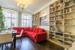 Une bibliothèque dotée d’un canapé d’angle rouge, d’un plancher en bois et d’une étagère remplie de livres et d’objets décoratifs.