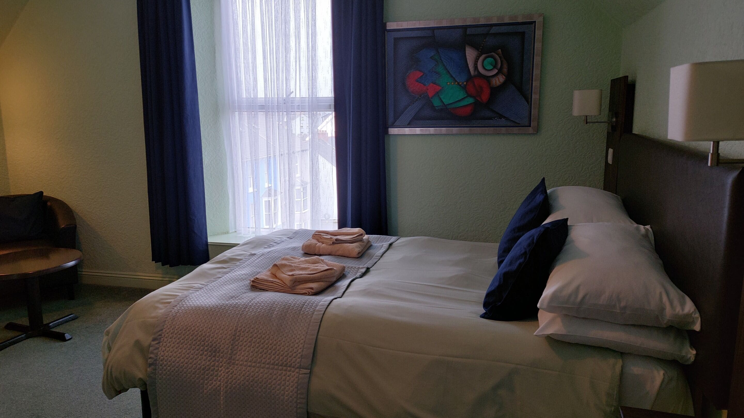 Een hotelkamer met een bed, een stoel, een schilderij aan de muur en een raam met gordijnen.