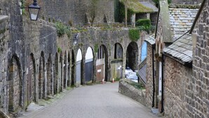 A narrow cobblestone street flanked by stone buildings with arched doorways and a lantern post.