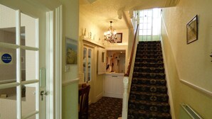 A hallway with a patterned carpet, a reception desk, a chandelier, and a staircase with a patterned carpet.