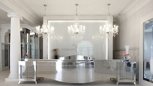 A modern reception area with a curved reception desk, large chandeliers, and a glass partition with the name "TERMES D'ORION". - Hotel Balneari Termes Orion (Santa Coloma de Farners)