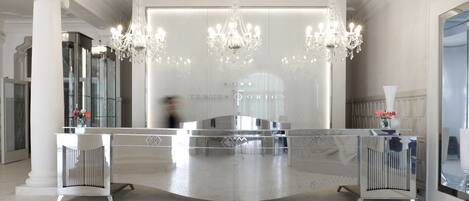 Una moderna zona de recepción con un mostrador curvo, grandes candelabros y un separador de vidrio que muestra el nombre "TERMES D'ORION".