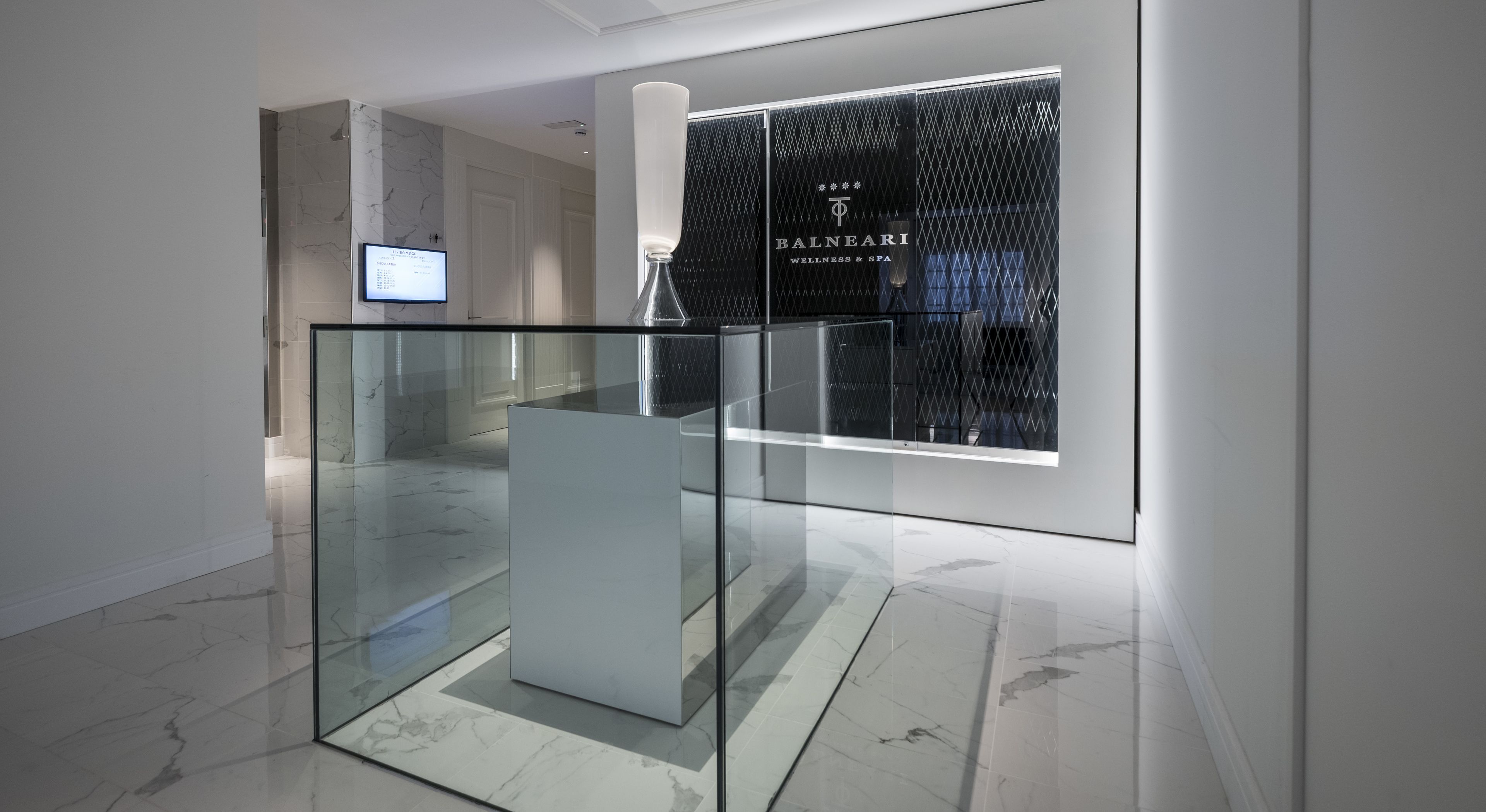 Un interior moderno con barandilla de cristal, suelo de mármol y un letrero de Balneari Wellness & Spa.