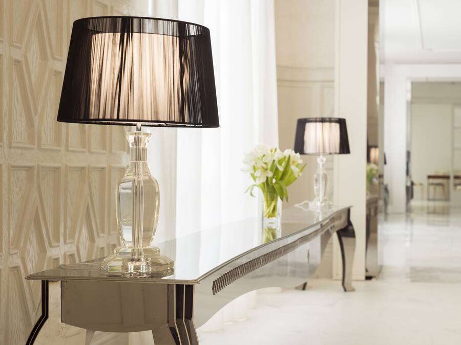 Ein modernes Interieur mit einem spiegelnden Tisch, der eine Lampe und eine Vase mit Blumen zeigt.