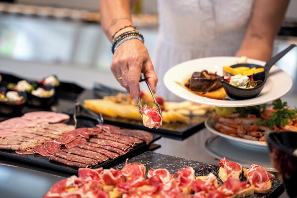 Ein Buffet mit verschiedenen Fleischsorten und einer Person, die Speisen austeilt.