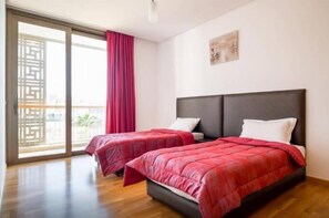 A hotel room with two beds, a large window with a view, and a sliding door to the balcony.