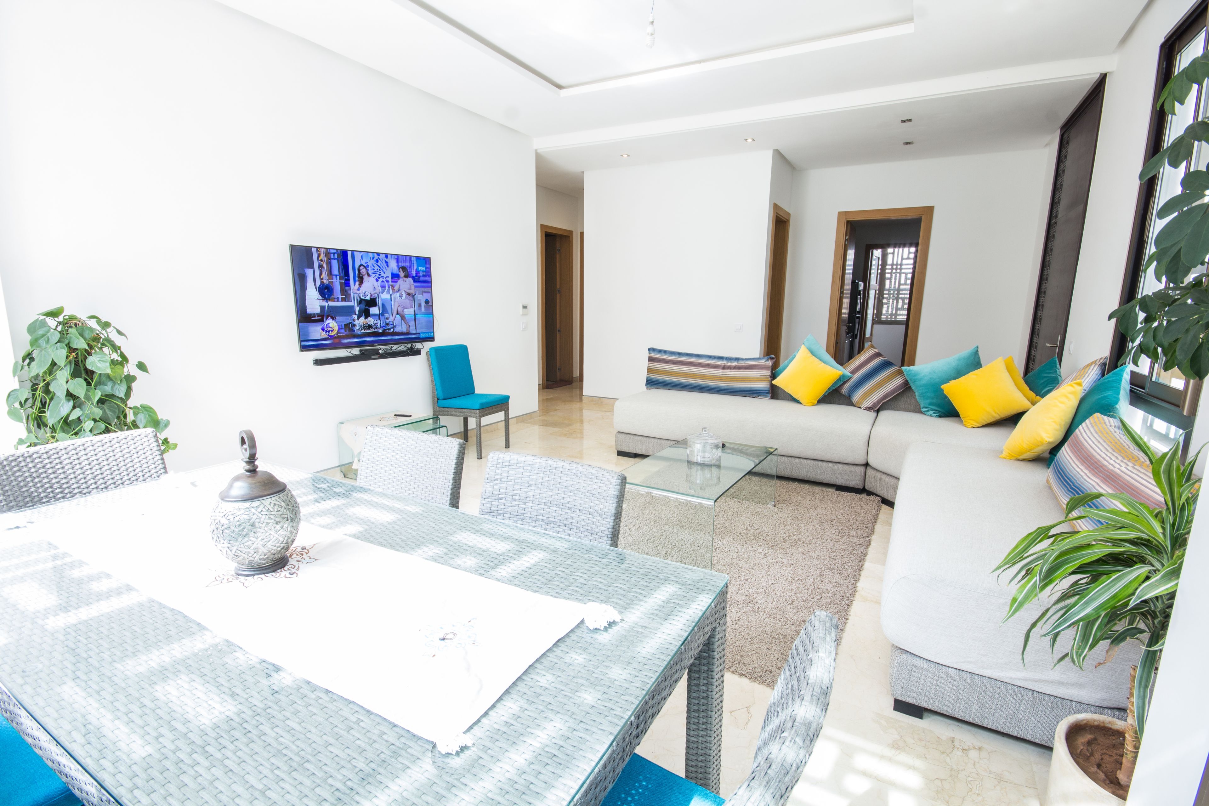 Una sala de estar moderna con un sofá, sillones, una mesa de centro de vidrio y un televisor montado en la pared.