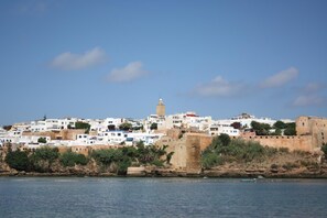 A coastal town with white buildings, a prominent tower, and a fortified wall along the shoreline.